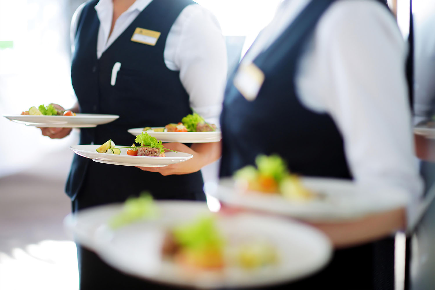 Two servers delivering plates of food to the table.